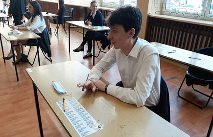 Zdjęcie maturzystów siedzących w przy szkolnych ławkach na sali gimnastycznej 