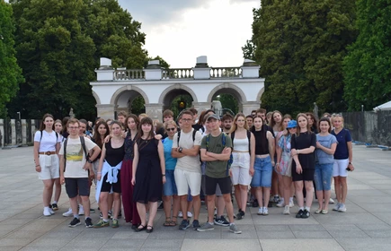 uczniowie stojący na tle pomnika w parku