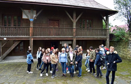 Grupowe zdjęcie uczestników wycieczki przy drewnianym domu 
