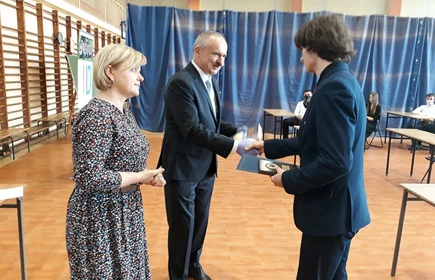 Na zdjęciu nauczyciele wręczający świadectwo uczniowi 