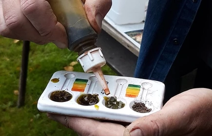 Na zdjęciu plastikowy pojemnik z ziemią, do którego wlewana jest specjalna substancja 