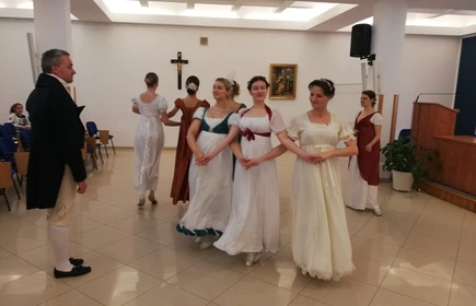 Na zdjęciu kobiety oraz mężczyźni tańczący  w strojach z epoki