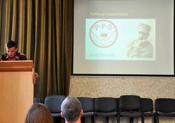 Zdjęcie prezentuje: osobę, która daje wykład, na ekranie Józef Piłsudski.