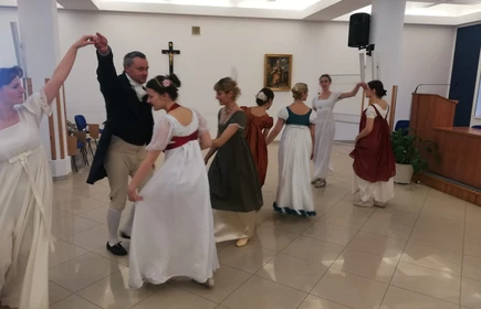 Na zdjęciu kobiety oraz mężczyźni tańczący  w strojach z epoki