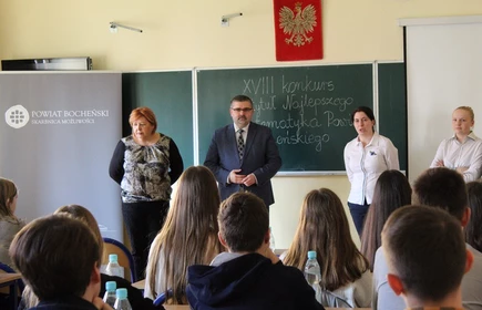 Nauczyciele stojący przy tablicy oraz siedzący uczniowie