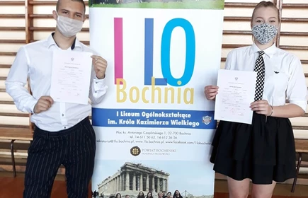 Dwójka uczniów przy plakacie 1 LO trzymająca świadectwa 