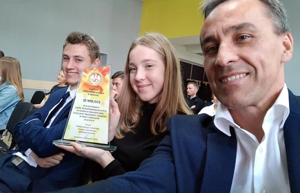 Zdjęcie przedstawia trzy osoby, jedna trzyma trofeum 1 LO