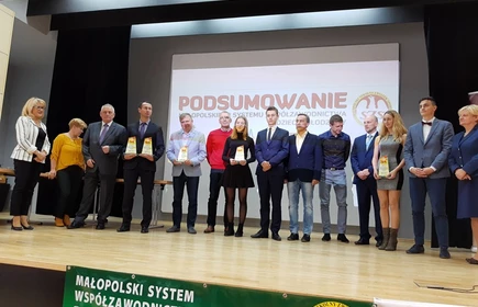 Zdjęcie przedstawia osoby stojące na scenie wraz z trofeami