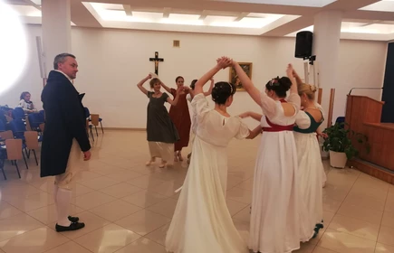 Na zdjęciu kobiety oraz mężczyźni tańczący  w strojach z epoki