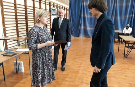 Na zdjęciu nauczyciele wręczający świadectwo uczniowi 