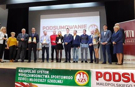 Zdjęcie przedstawia osoby stojące na scenie wraz z trofeami