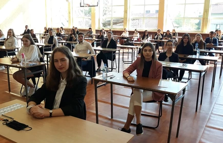 Zdjęcie maturzystów siedzących w przy szkolnych ławkach na sali gimnastycznej 