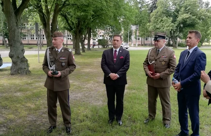 Zdjęcie oficjeli wraz z żołnierzami stojącymi na łące  