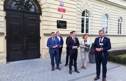 Osoby przemawiają przed drzwiami 1LO