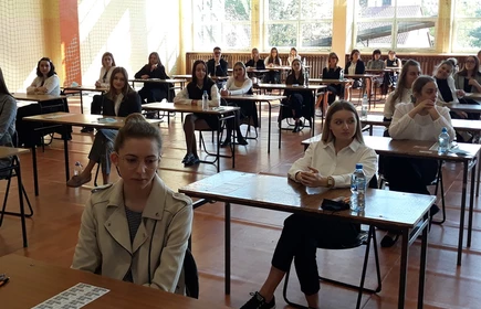 Zdjęcie maturzystów siedzących w przy szkolnych ławkach na sali gimnastycznej 
