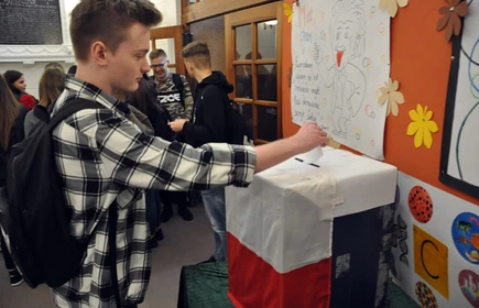 Na zdjęciu uczeń wrzucający kartę wyborczą do urny wyborczej