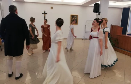 Na zdjęciu kobiety oraz mężczyźni tańczący  w strojach z epoki