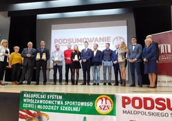 Zdjęcie przedstawia osoby stojące na scenie wraz z trofeami