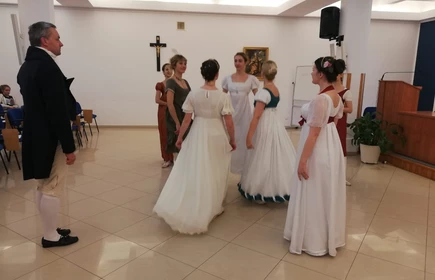 Na zdjęciu kobiety oraz mężczyźni tańczący  w strojach z epoki